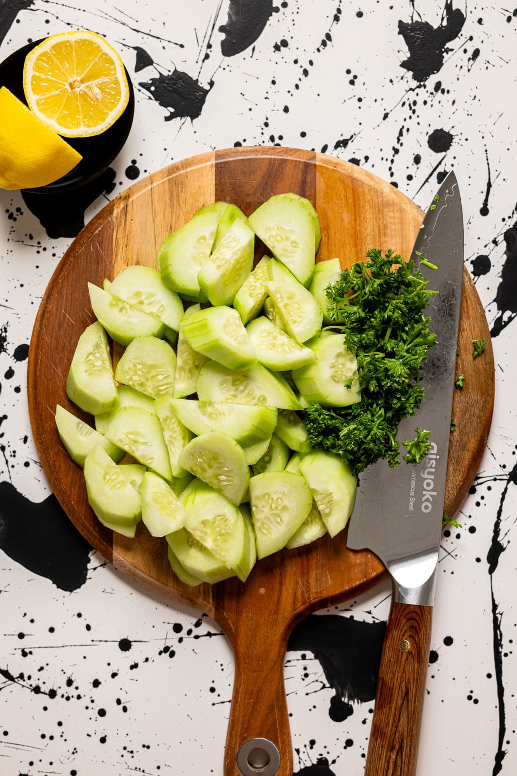 Cucumber and parsley chopped on a cutting board with a knife.