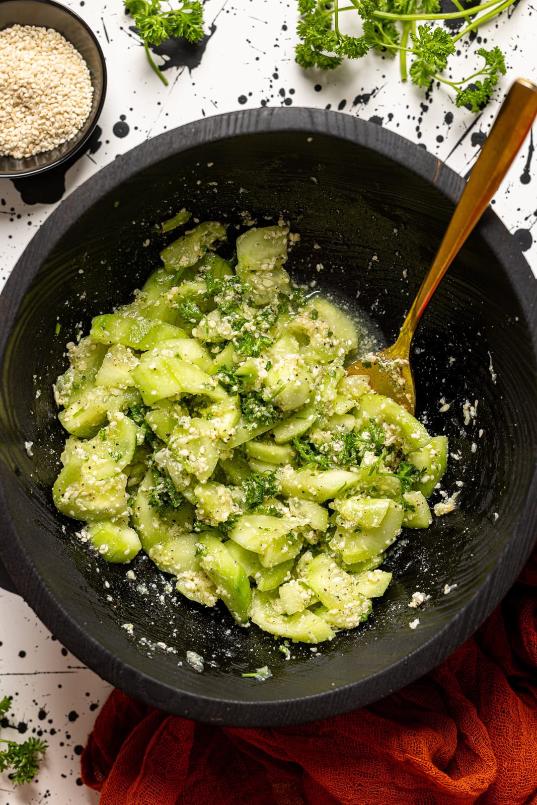 Cucumber salad in a black bowl with a spoon and a red napkin.