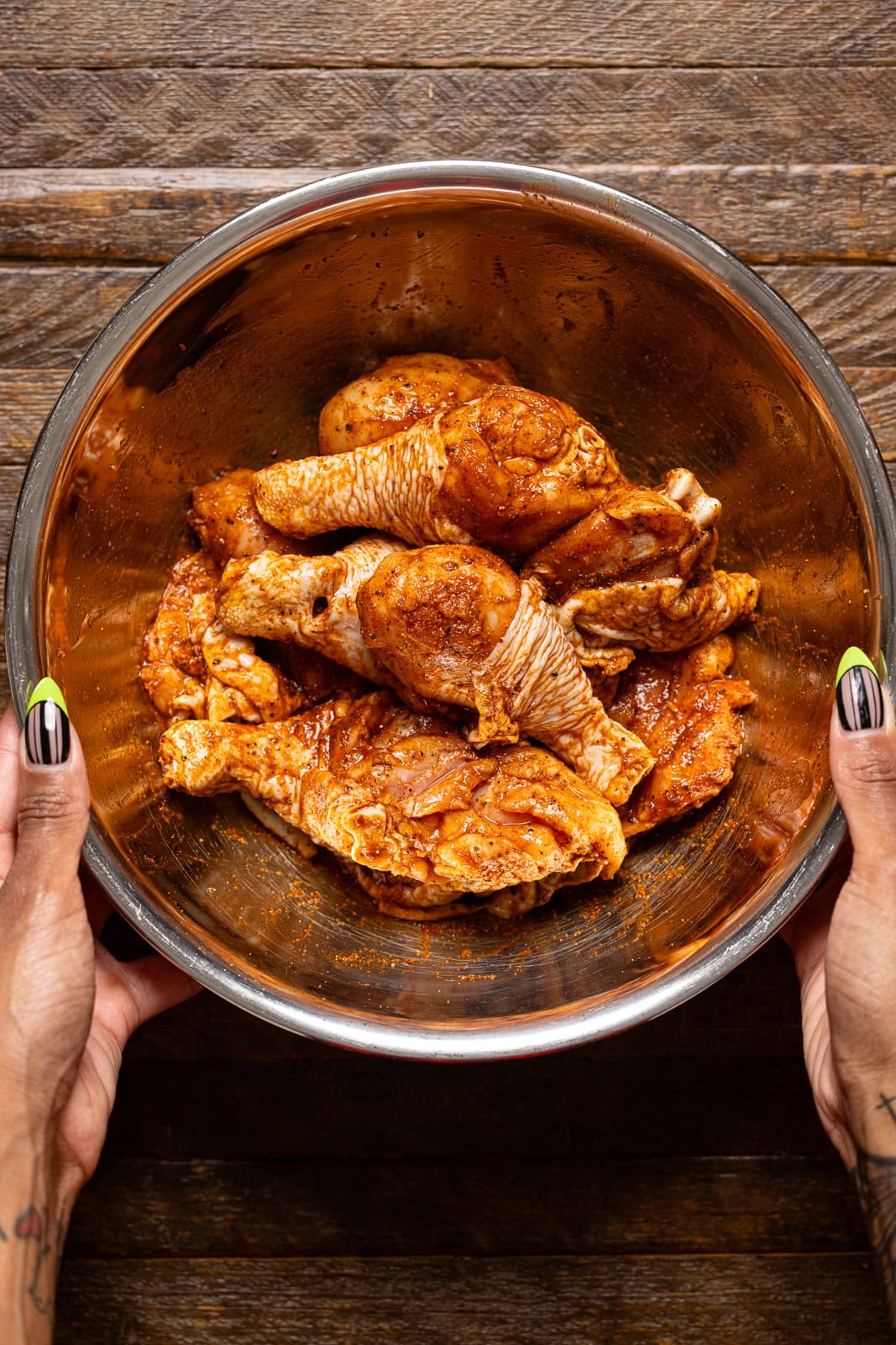 Seasoned chicken in a silver bowl being held.