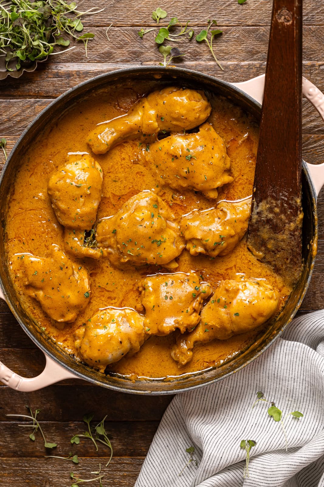 Smothered chicken in a white pot with a wooden spoon.