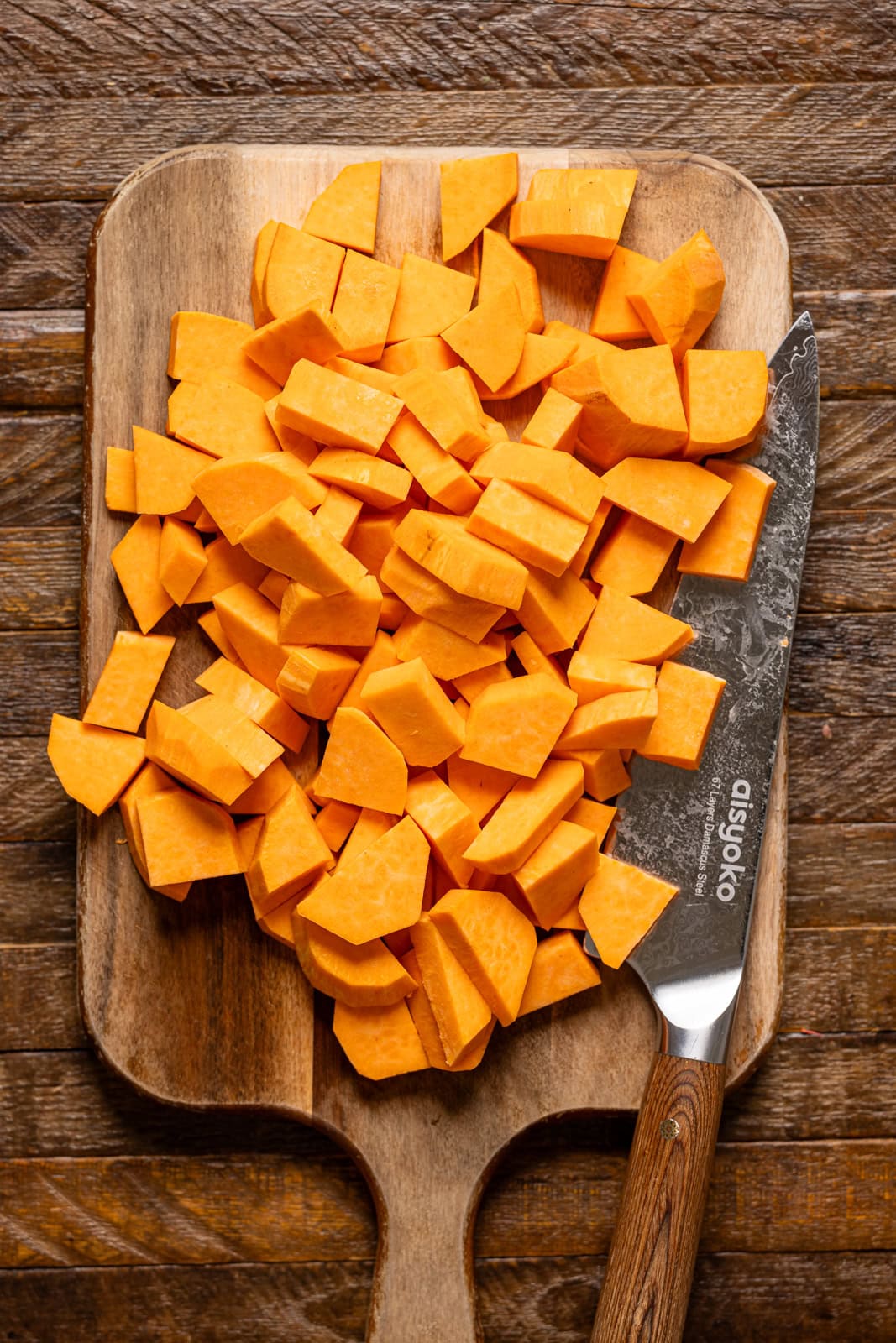 Chopped sweet potatoes on a cutting board with a knife. 