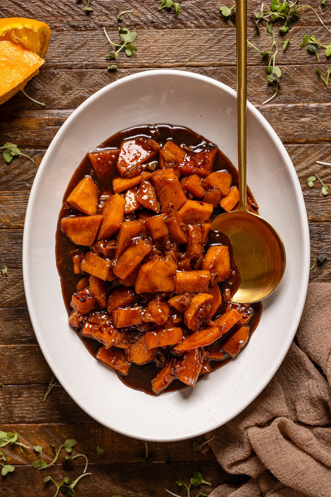 Cooked yams in a white platter with a spoon.