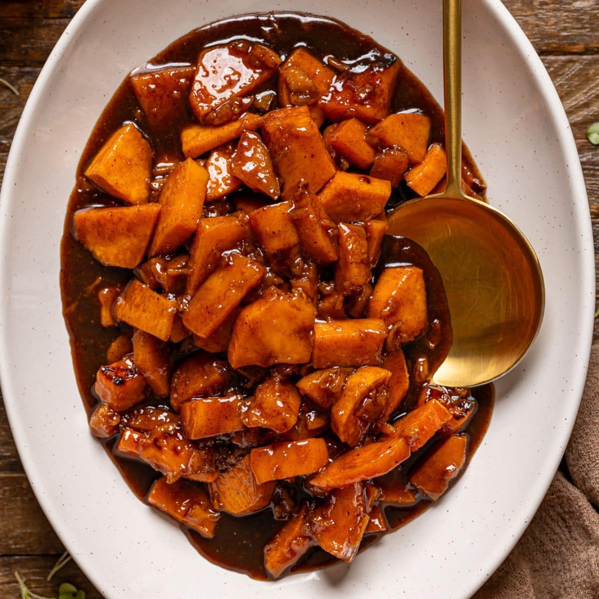 Cooked yams in a white platter with a spoon on a brown wood table.