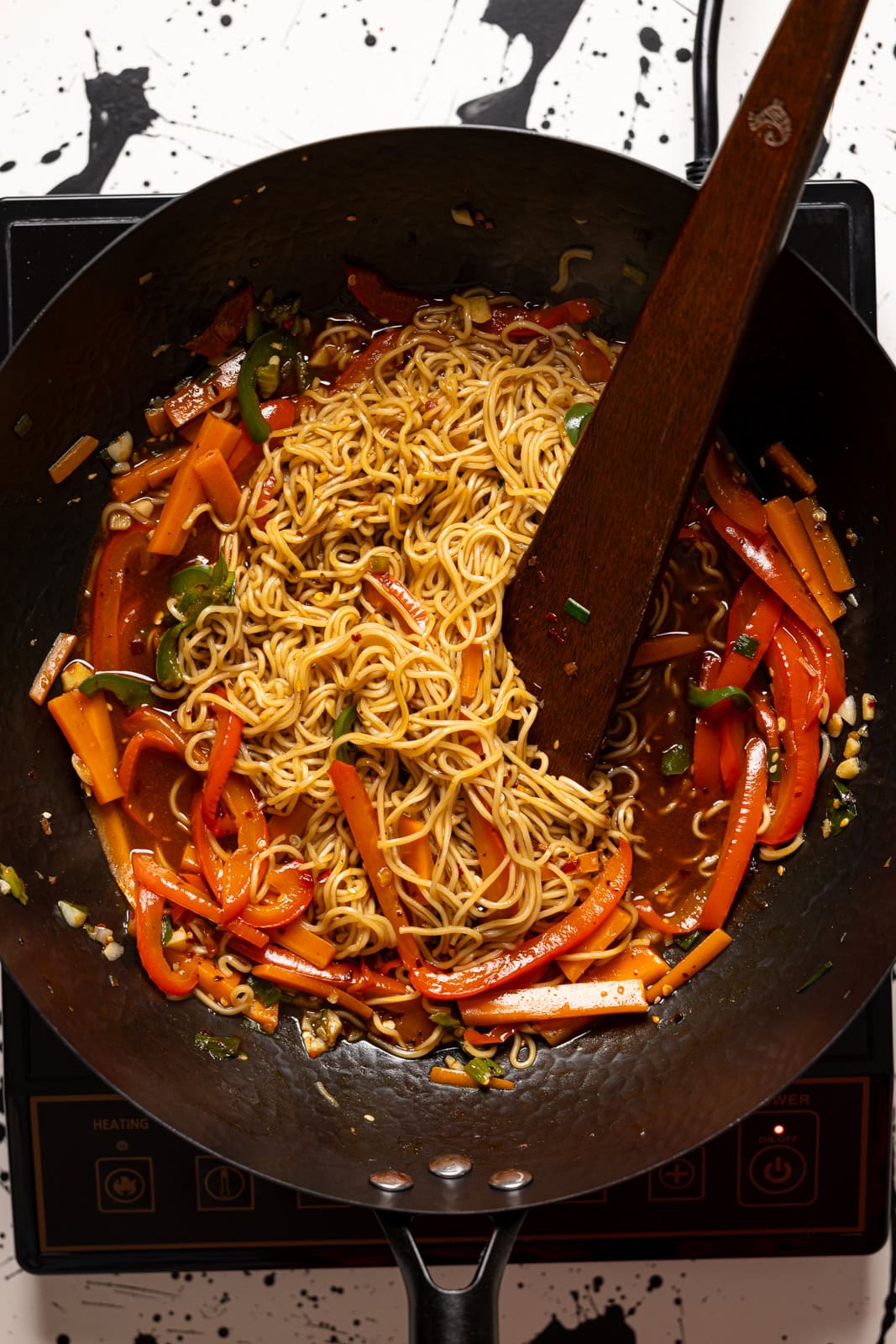 Ramen in a black wok with a wooden spoon.