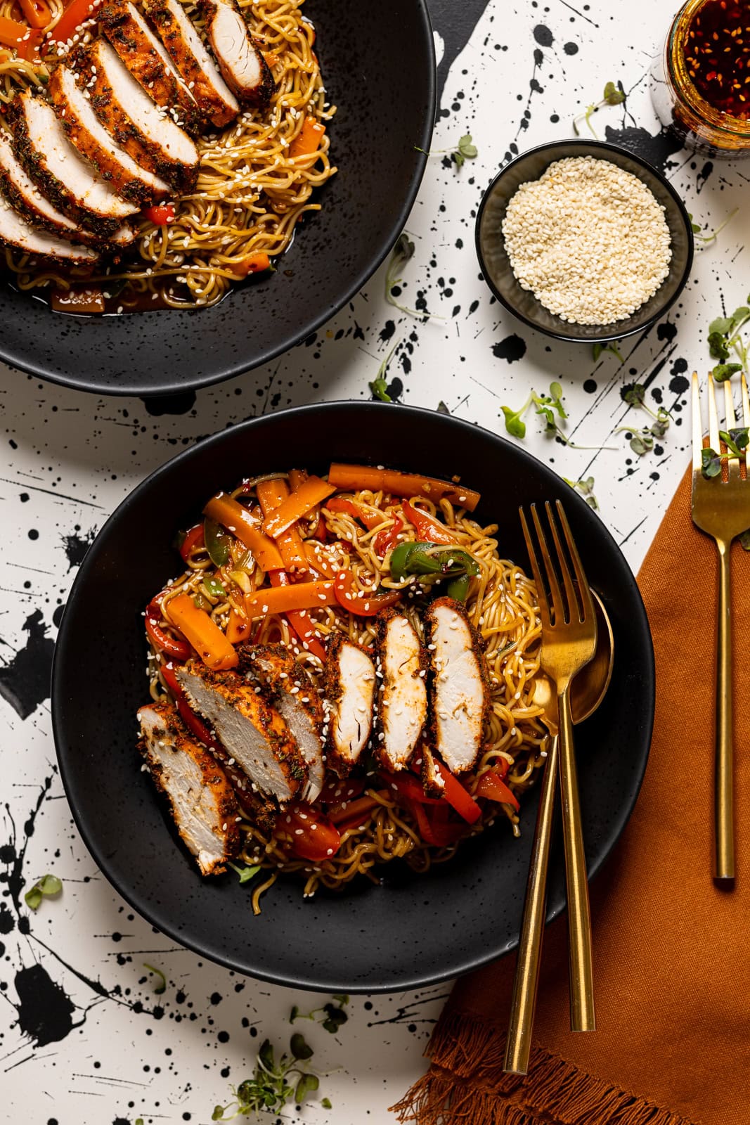Chicken ramen in two black bowls with forks and sesame seeds.