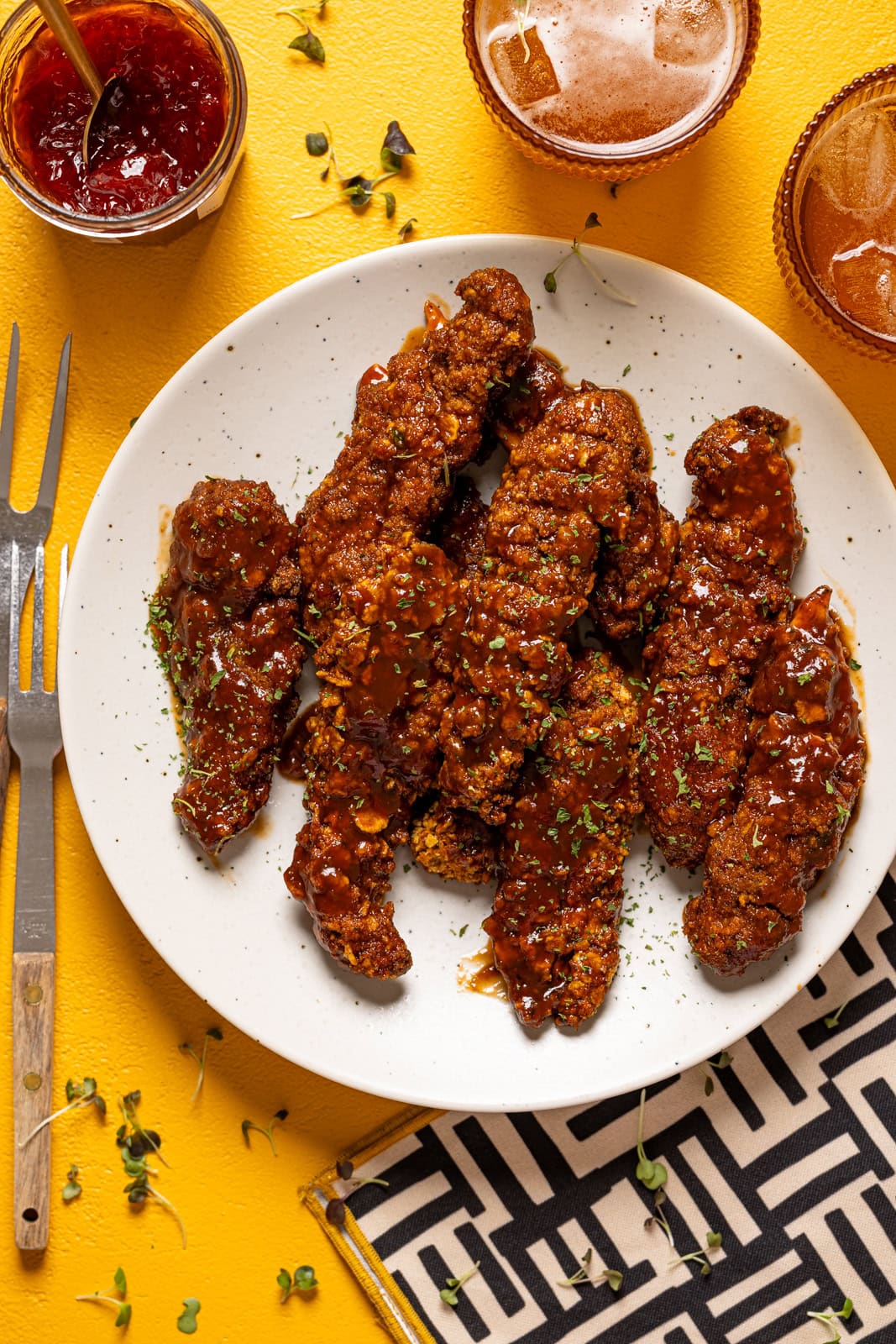 BBQ chicken tenders on a white plate on a yellow table.