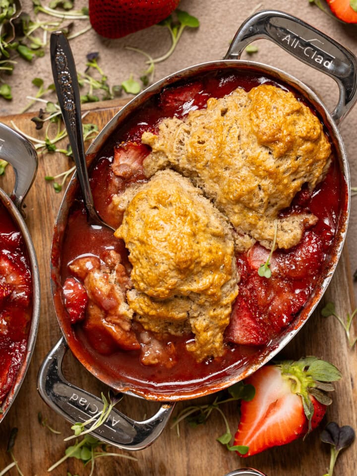 Up close shot of strawberry cobbler in a metal bakeware with a spoon and strawberries.