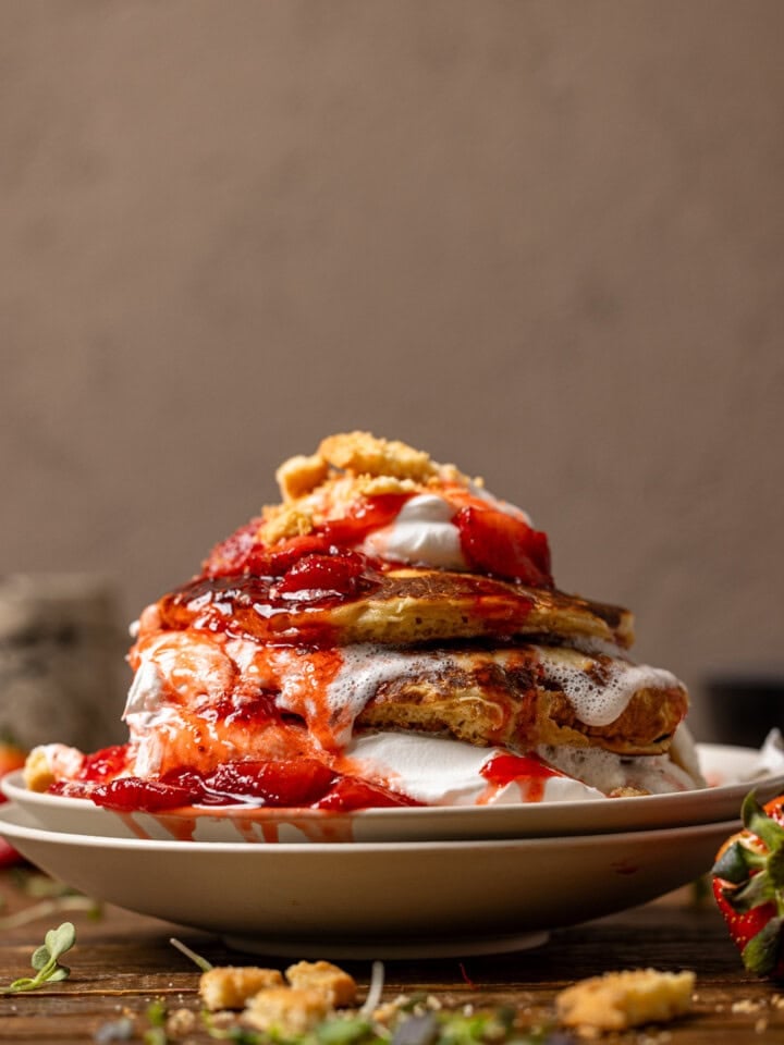Stacks of pancakes with whipped cream, strawberries, and cookies.