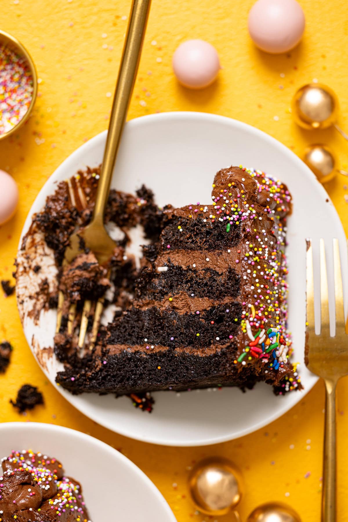 Up close shot of slice of cake on a white plate with two forks and sprinkles.