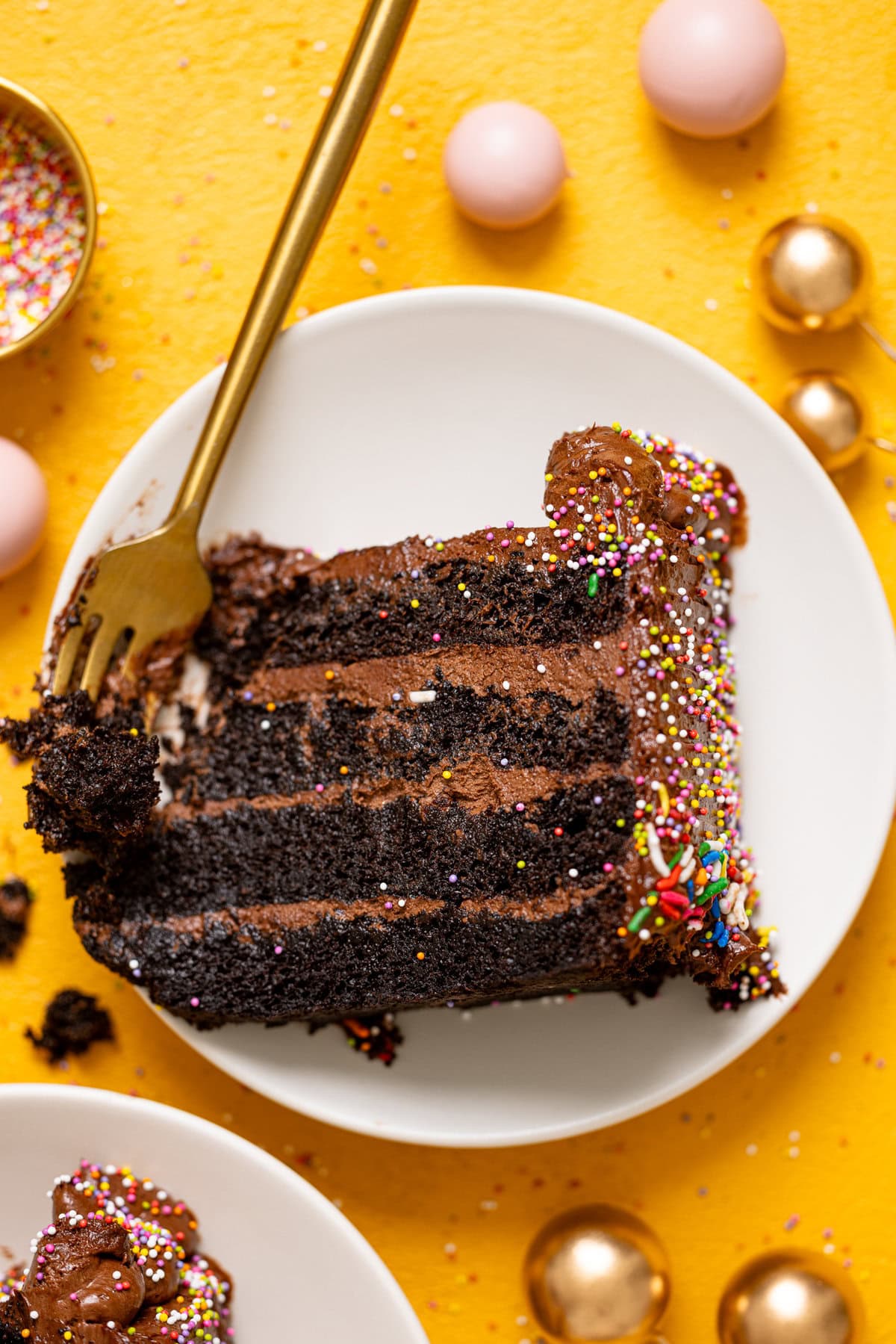 Up close shot of chocolate cake slice on a white plate with a fork with balloons.