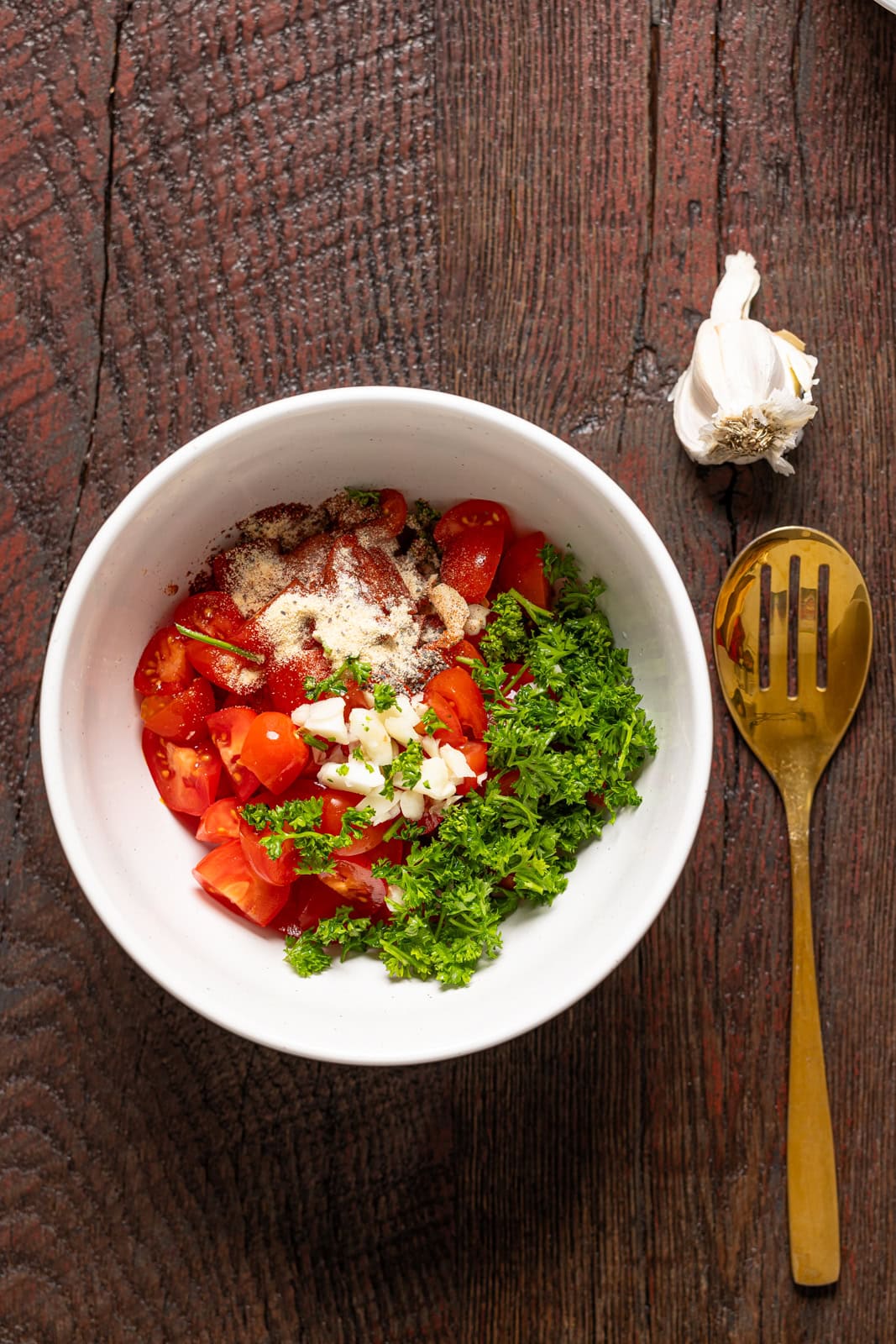 Bruschetta toppings in a bowl with garlic and a gold spoon.