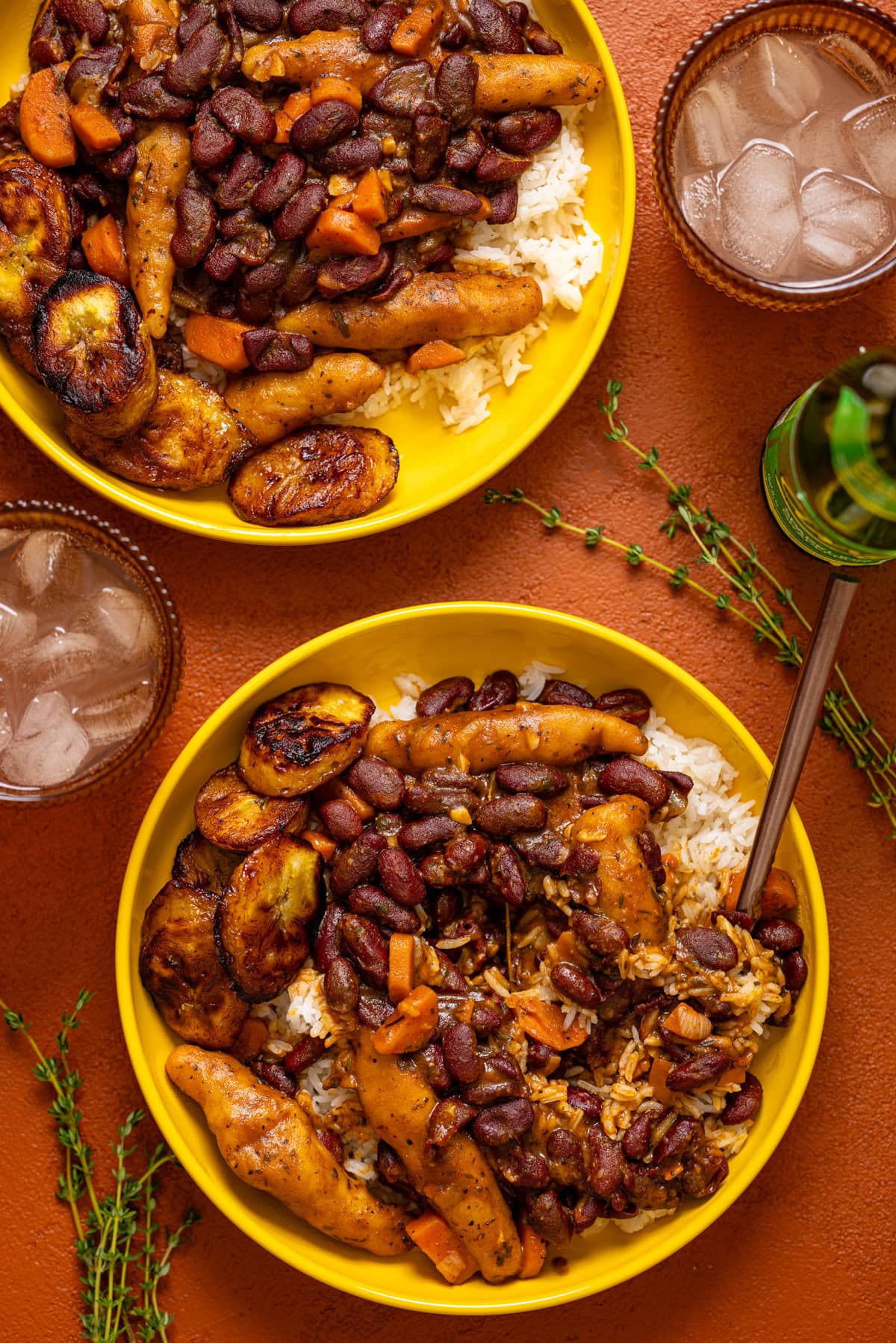 Two plates on food with friend plantain on a burgundy table with drinks.