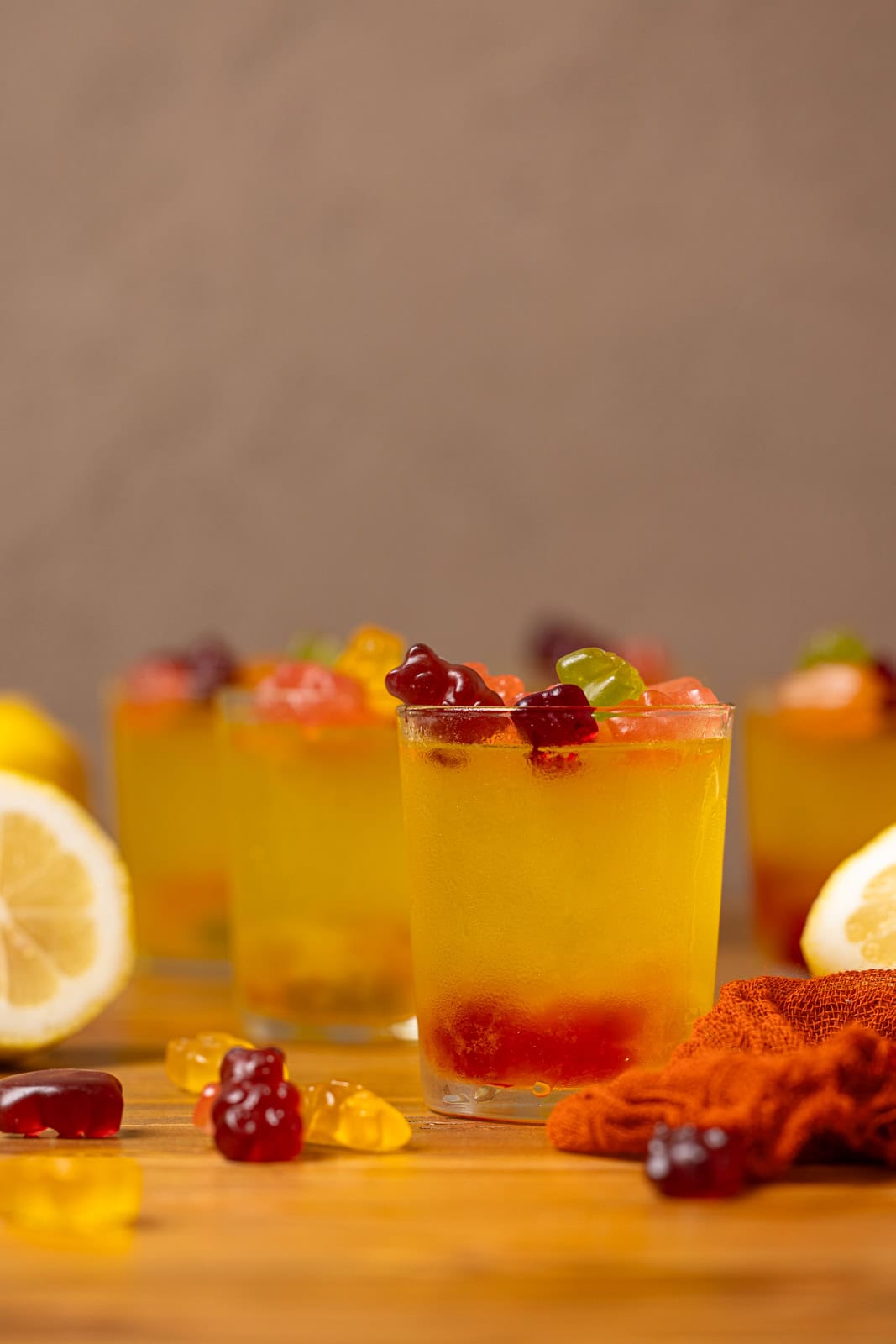 Lemon drop shots on a brown wood table with gummy bears and lemons.