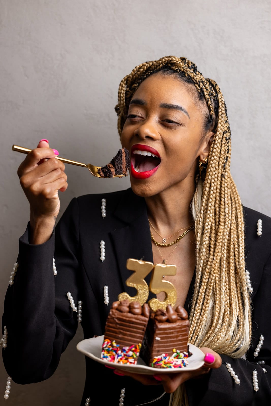 Shanika holding a slice of cake on a fork towards her mouth in a black/white suit.
