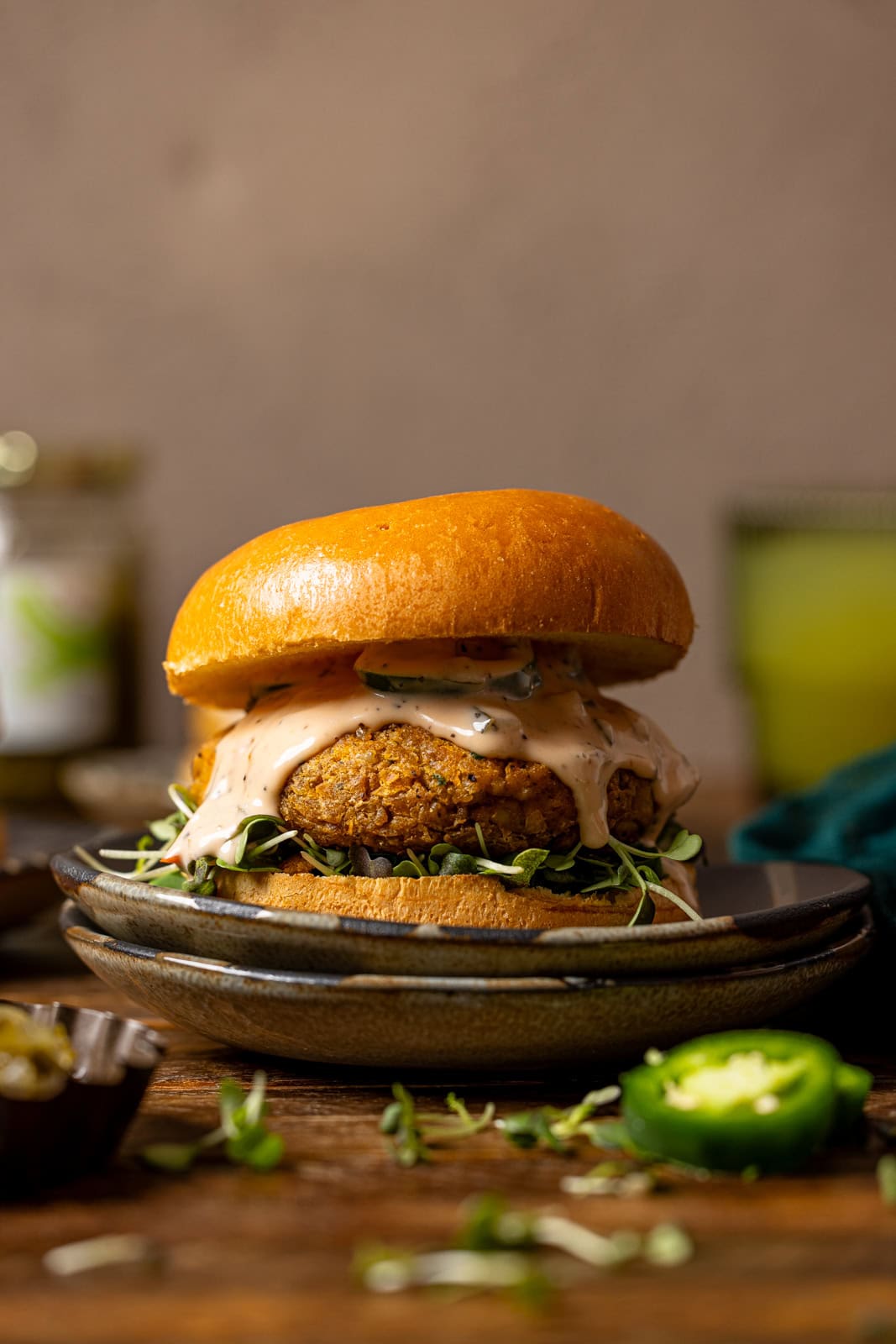 Veggie burger on two plates with a drink in the background and pickles.
