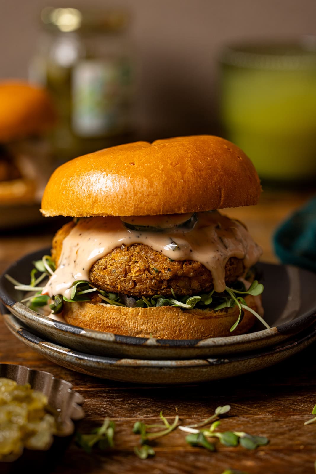 Veggie burger on two plates with a drink and pickles in the background.