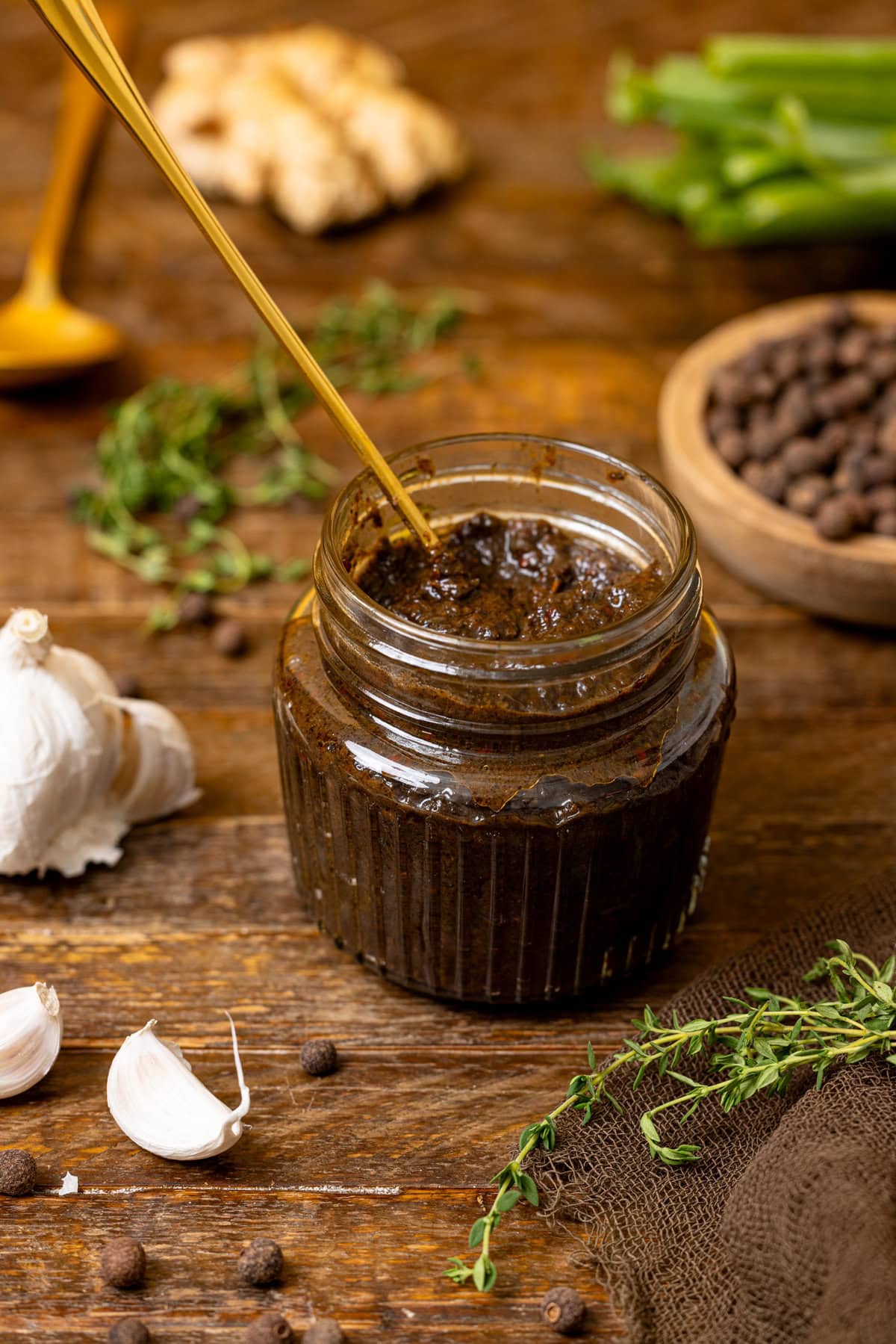 Jerk marinade on a brown wood table with garlic, thyme, and ingredients. 