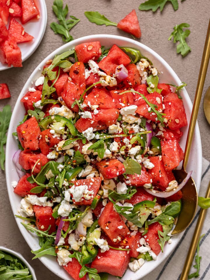 Salad in a white serving dish with gold spoons.