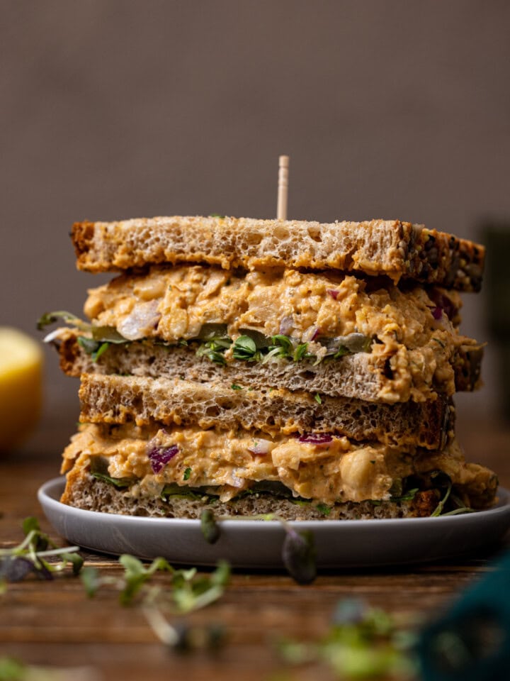 Up close shot of sandwiches stacked on a plate with a toothpick and a lemon.