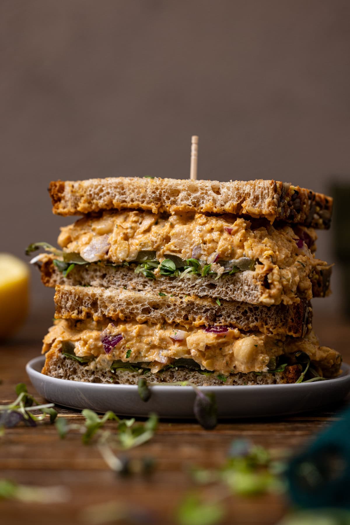 Up close shot of sandwiches stacked on a plate with a toothpick and a lemon.