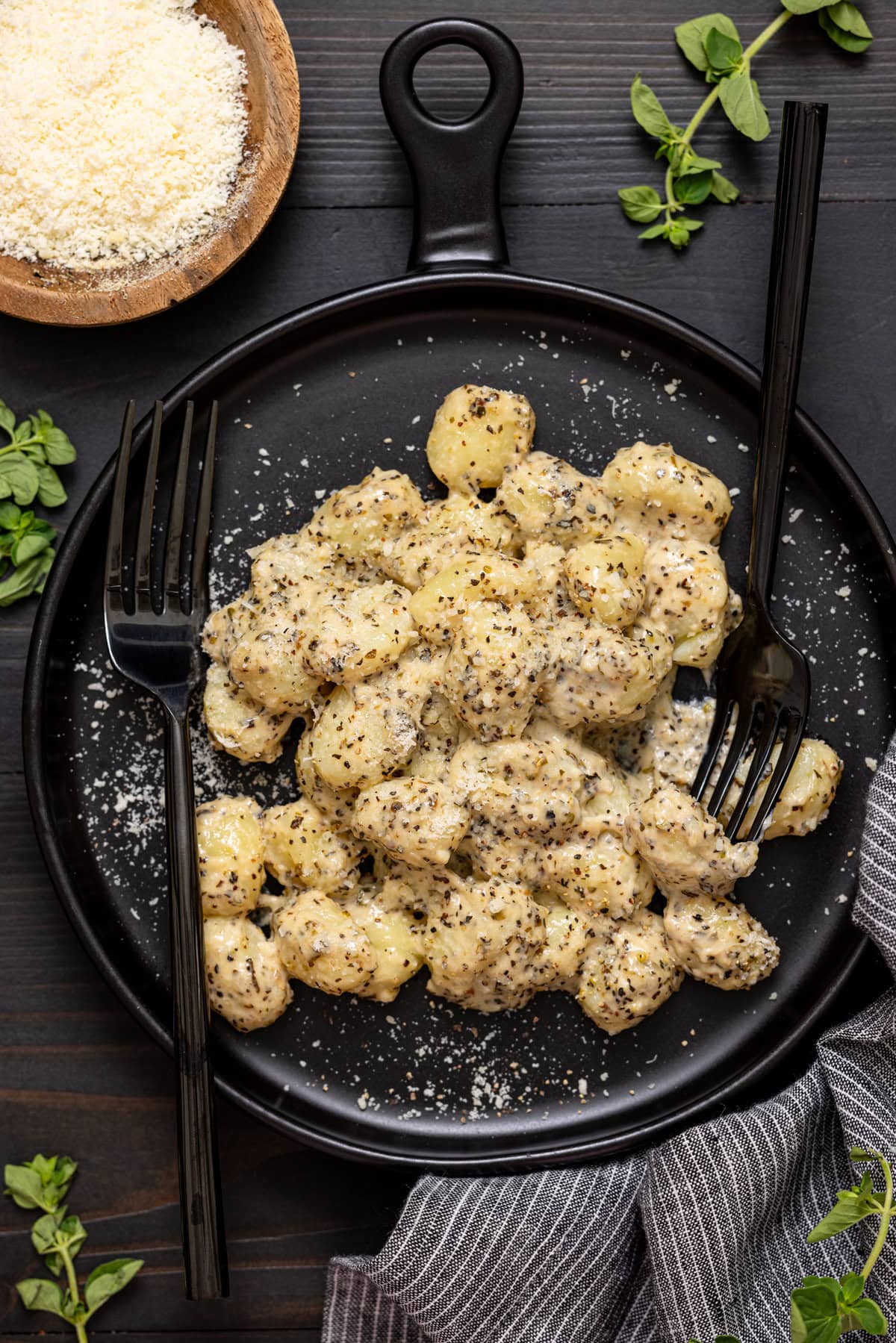 Up close shot of gnocchi on a black plate with two forks and grated parmesan.