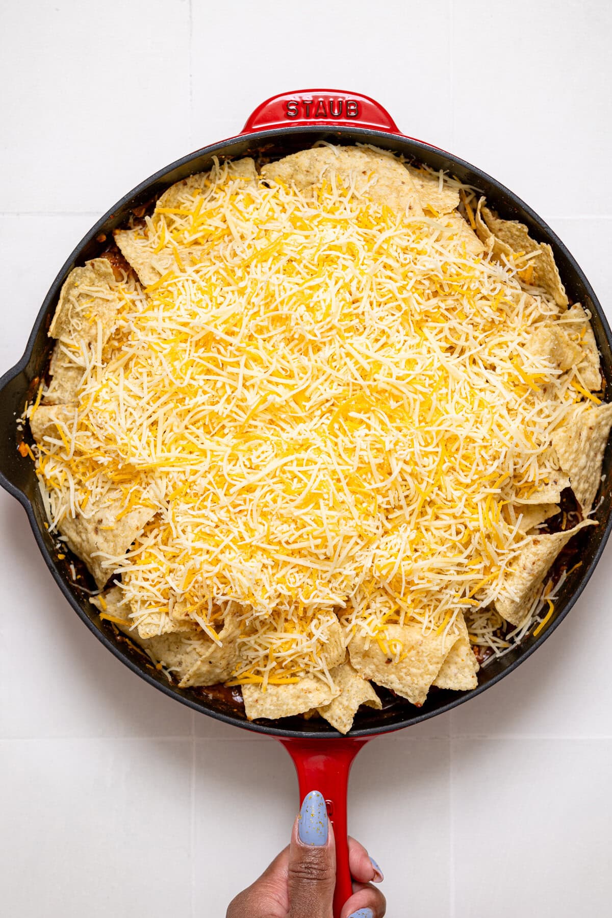 Cheese topped on a enchilada in red skillet being held.