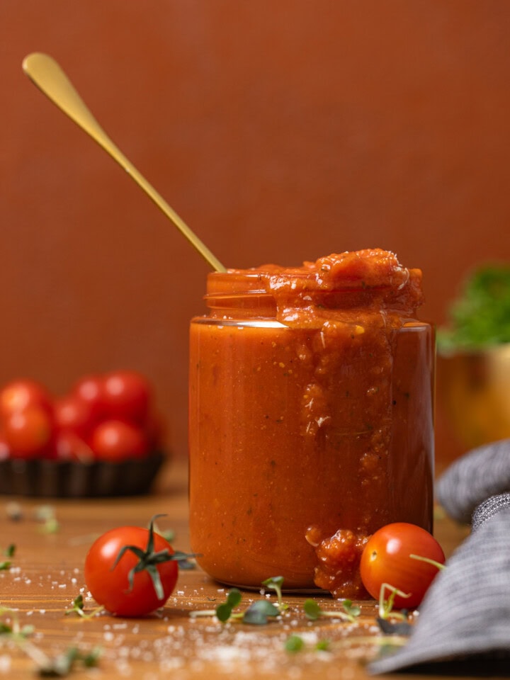 Vodka sauce in a jar with a spoon on a brown wood table with tomatoes.