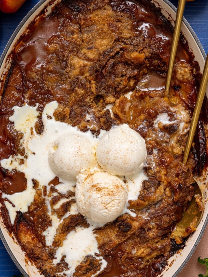 Peach dump cake in a baking dish with serving spoons and ice cream.