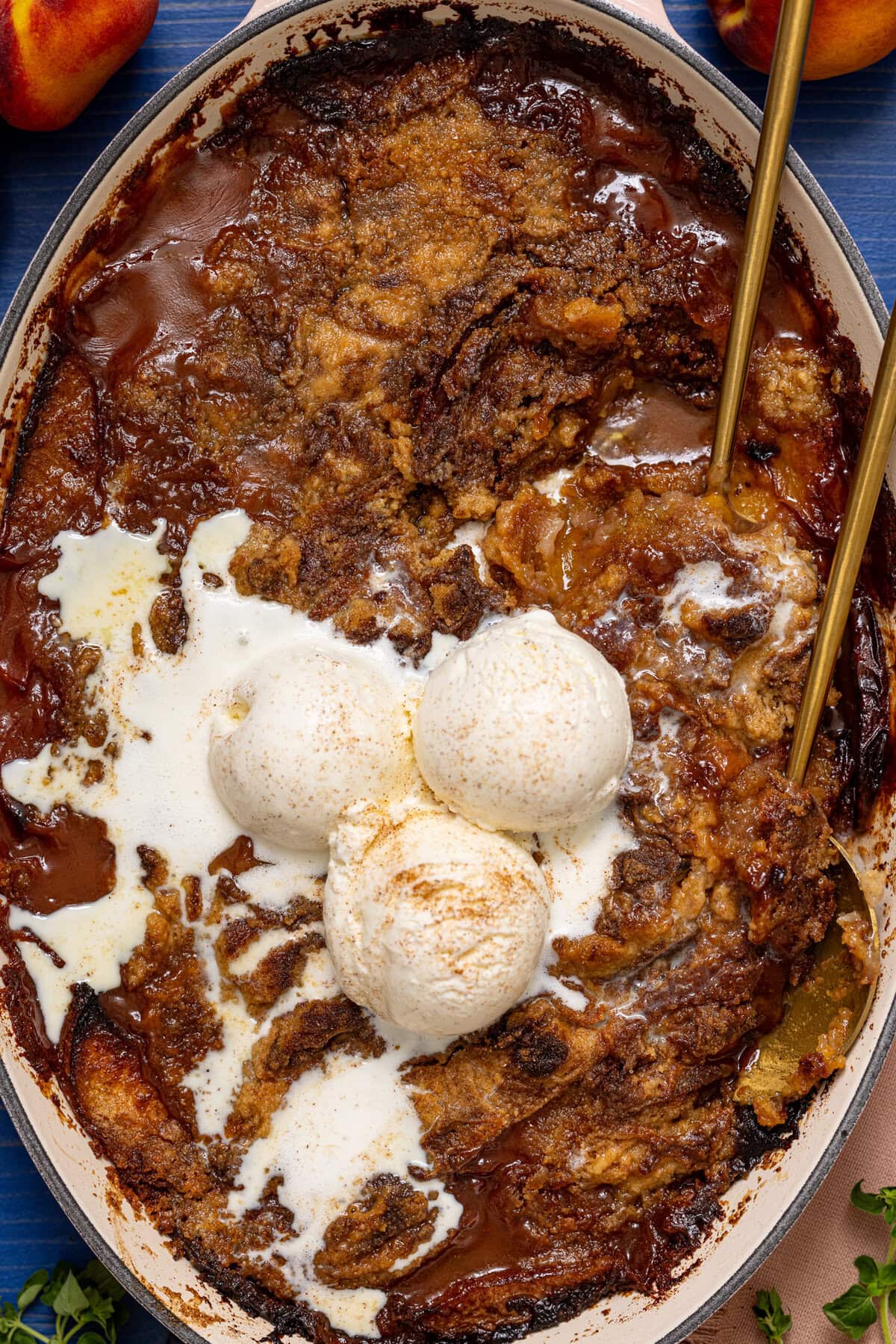 Peach dump cake in a baking dish with serving spoons and ice cream.