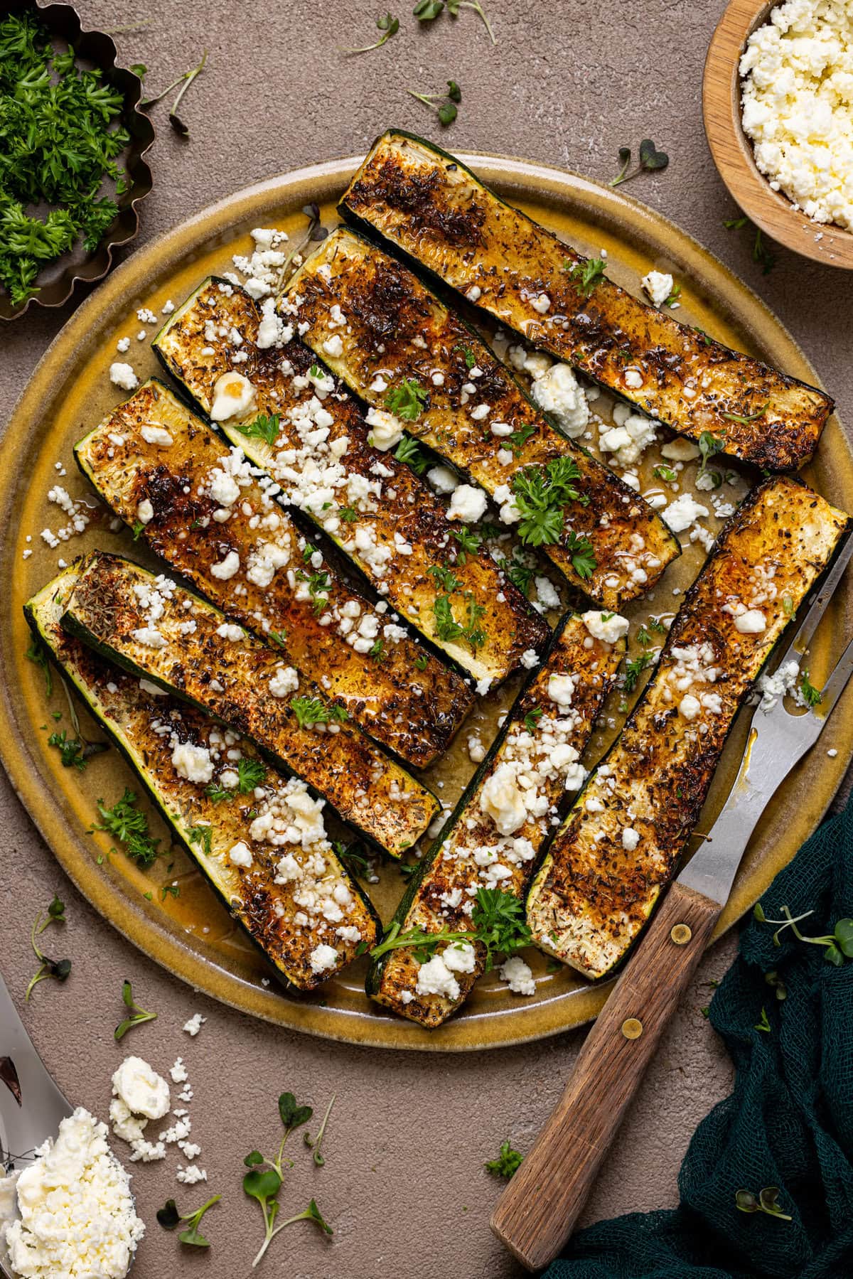 Roasted zucchini on a plate with a fork and feta cheese.