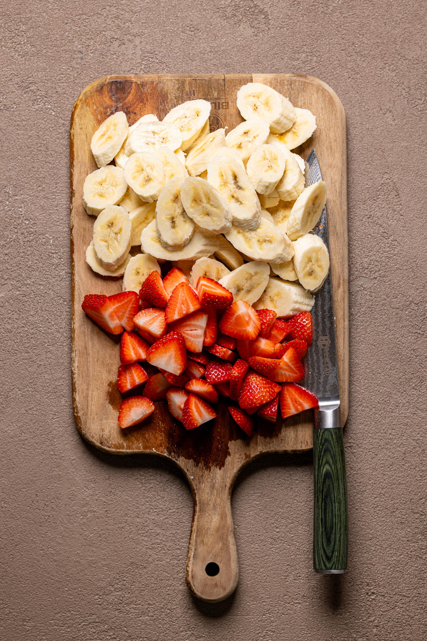 Image of chopped bananas and fresh strawberries on a cutting board with a knife.