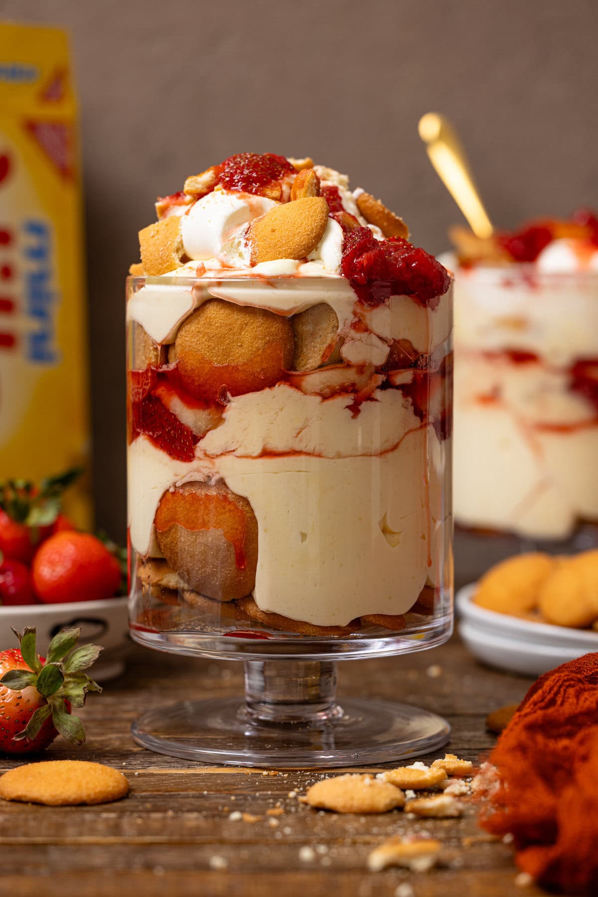 Two trifle bowls of strawberry banana puddings with a box of nilla wafers and strawberries in the background.