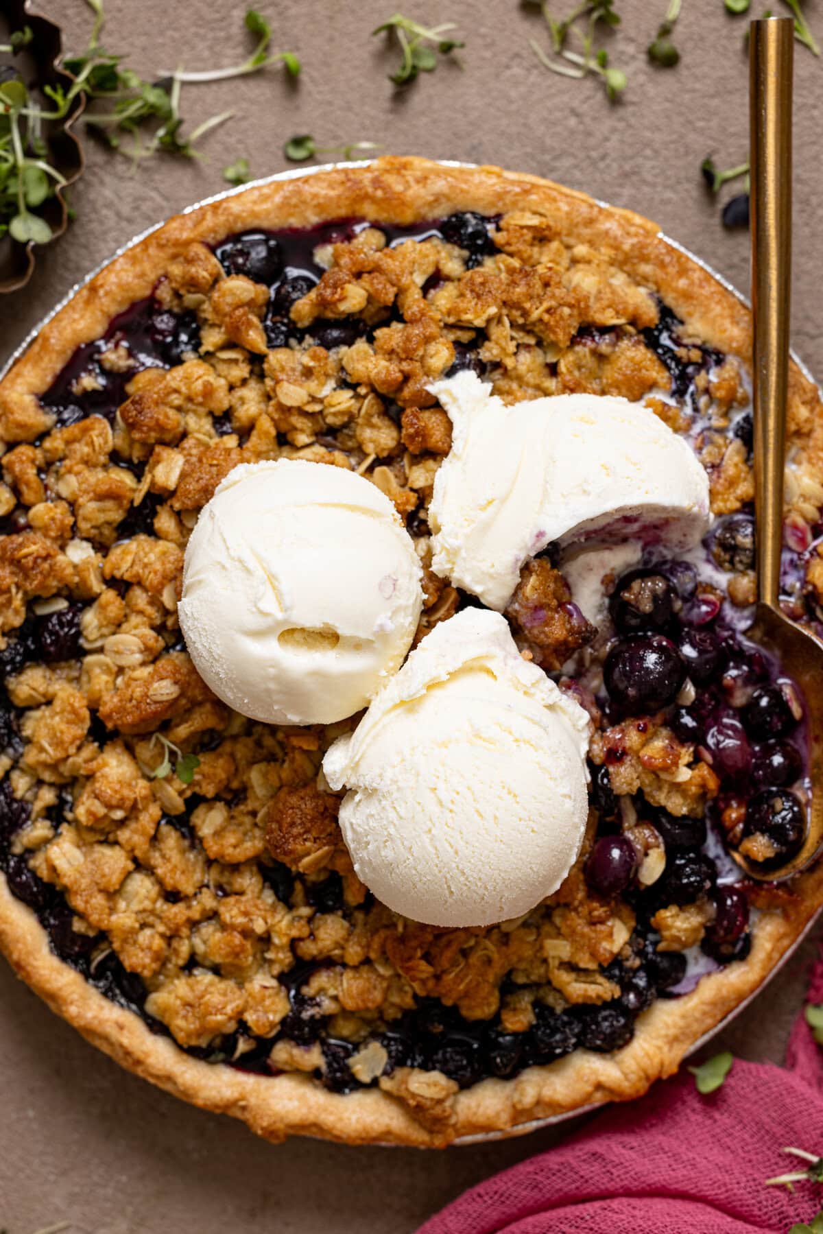 Blueberry crumble pie with scoops of vanilla ice cream and a spoon.