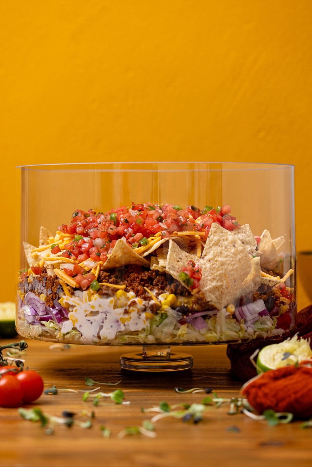 7-layer salad in a trifle bowl on a brown wood table with limes.