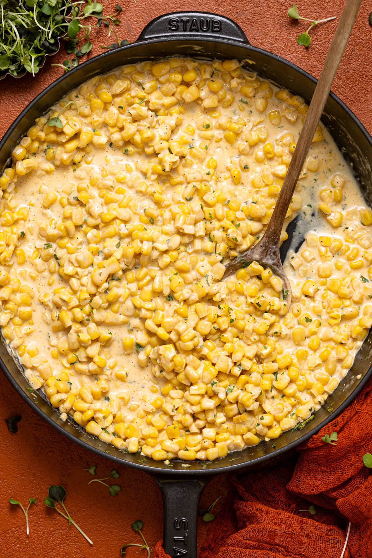 Creamed corn in a black skillet with a wooden spoon.