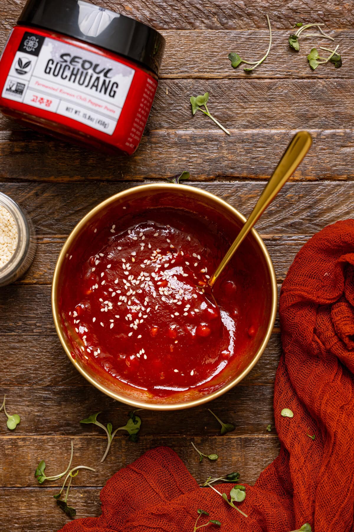 Gochujang sauce in a gold bowl with a spoon on a brown wood table.