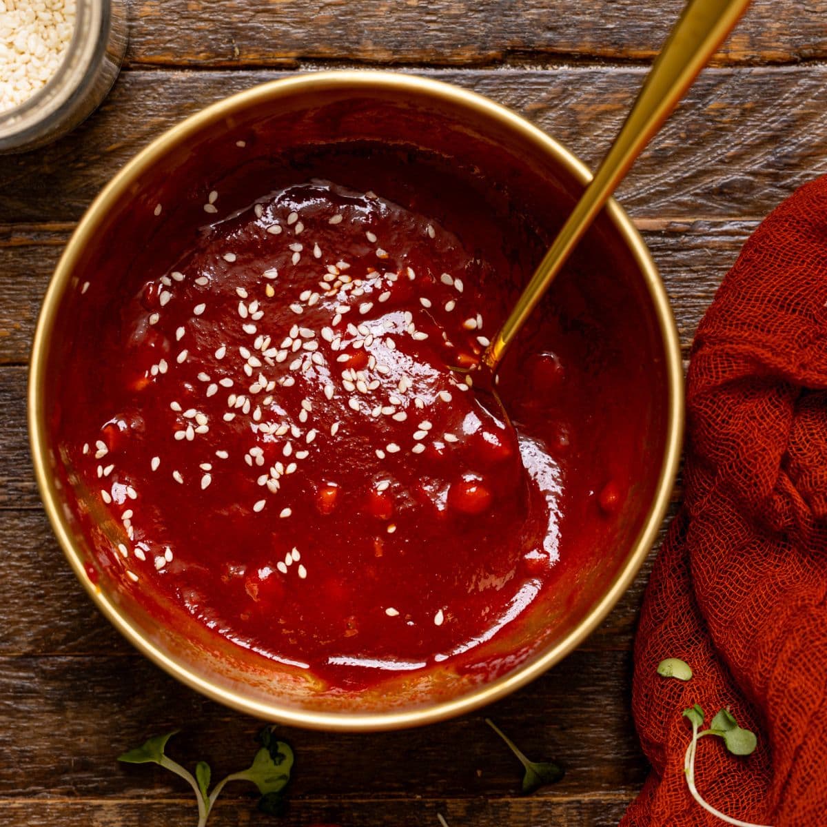 Gochujang sauce in a gold bowl with a spoon on a brown wood table.