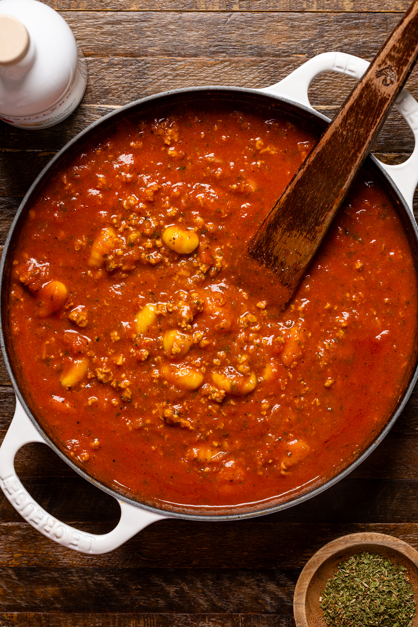 An image of bolognese sauce in a skillet with a wooden spoon.