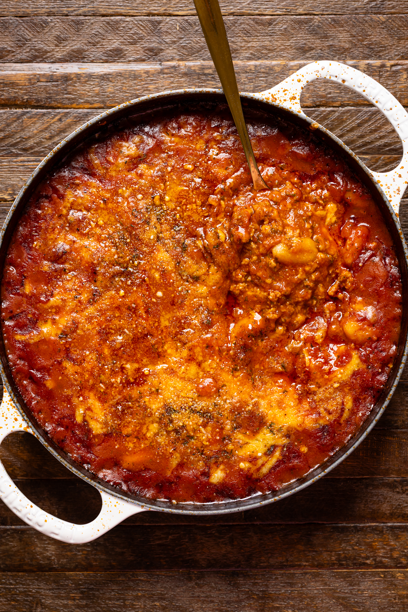 An image of the baked bolognese gnocchi in a skillet on a wood table.