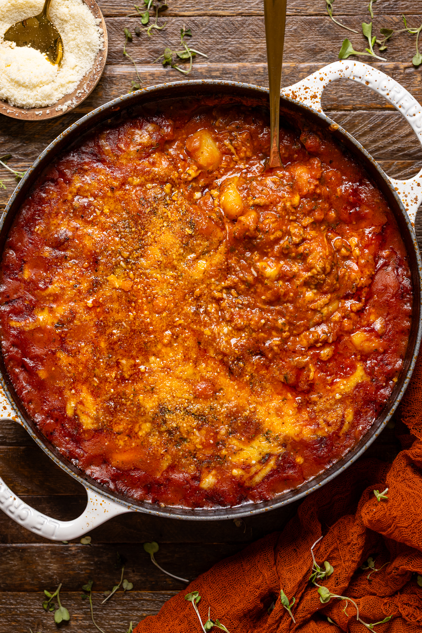 An image of baked bolognese gnocchi in a skillet with a spoon on a wood table.