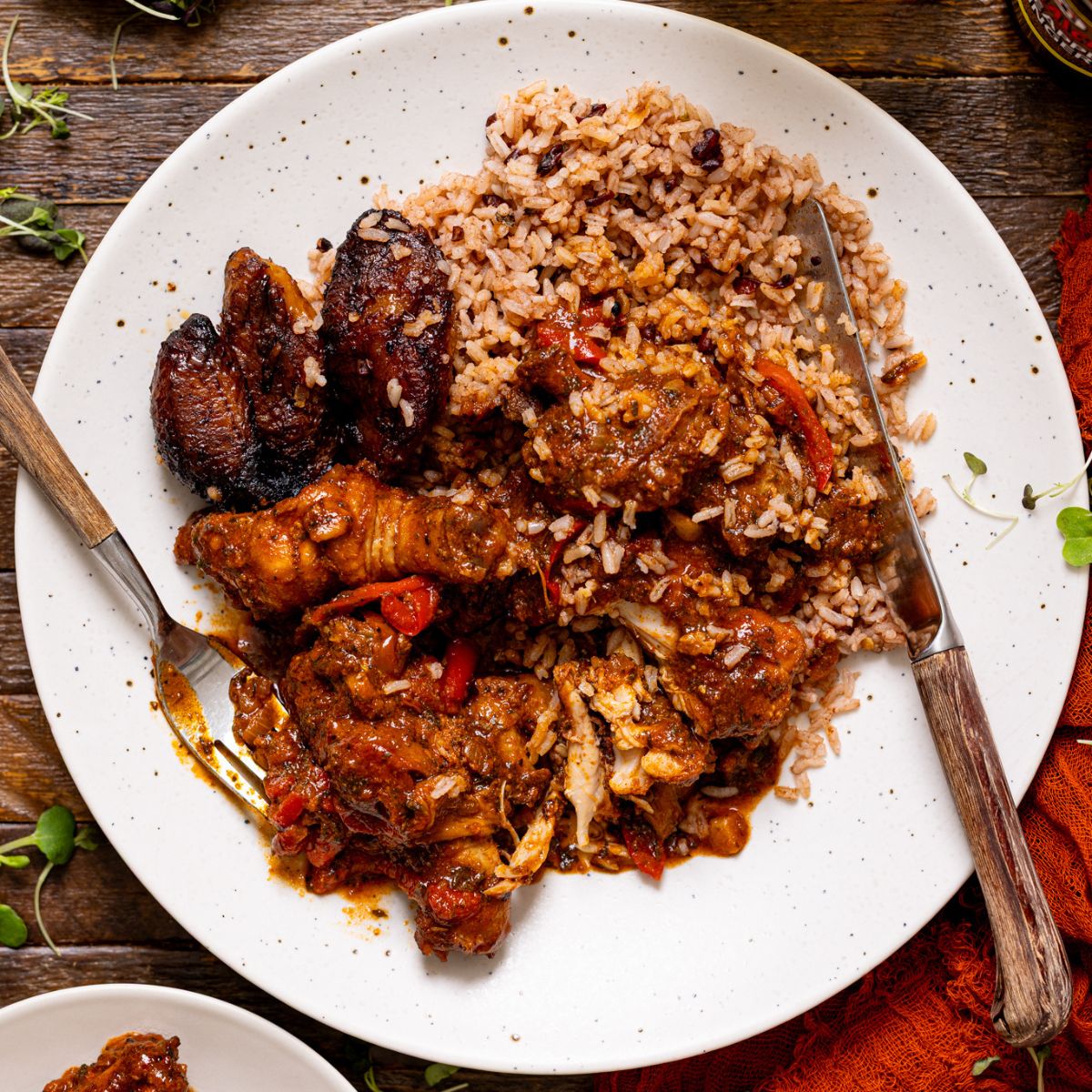 An image of a plate of stew chicken with rice and peas and fried plantain with forks.