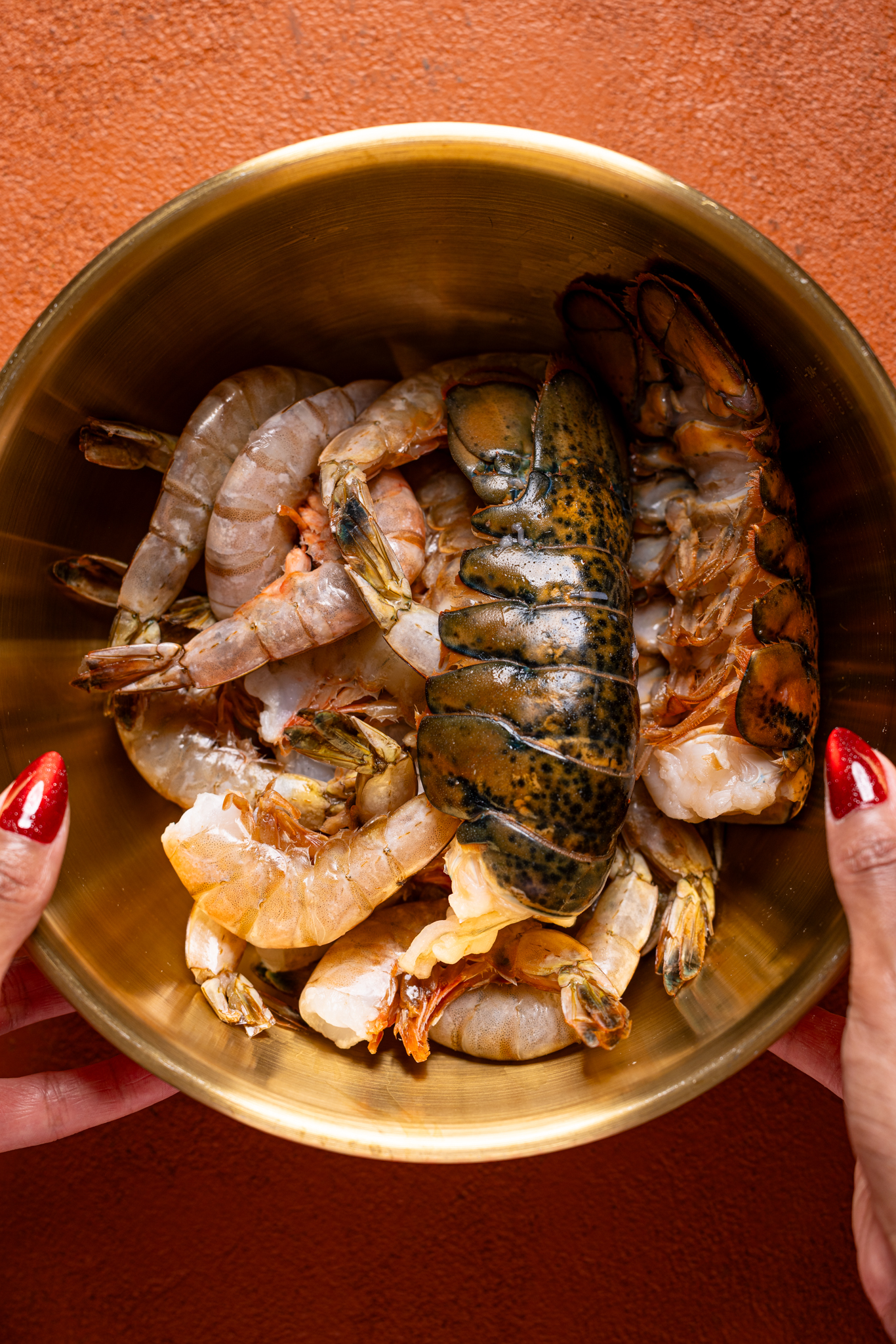 Image of raw seafood in a gold bowl being held with hands.
