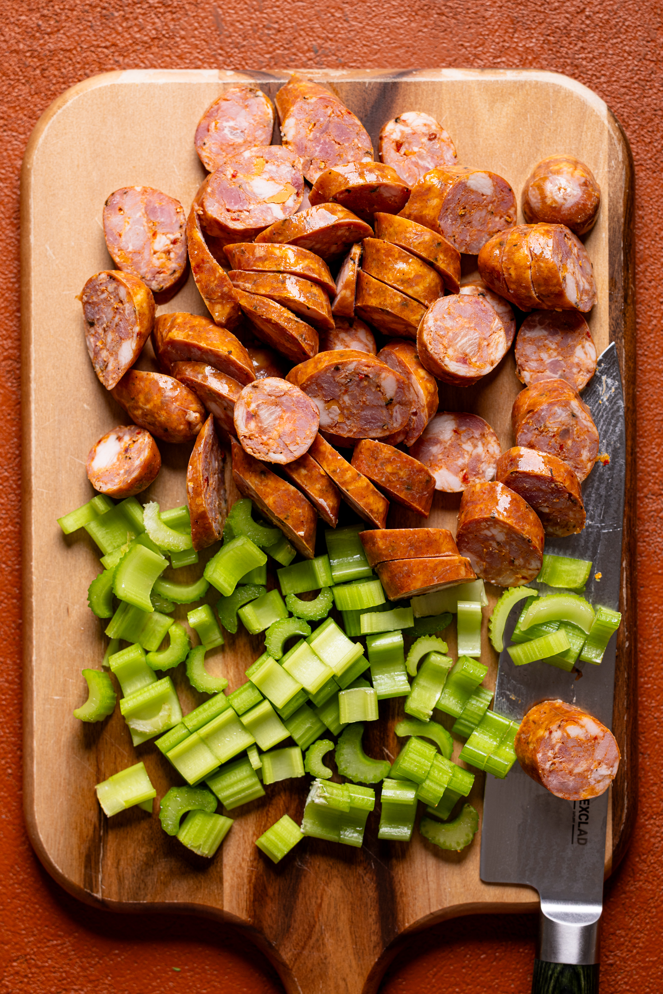 Image of chopped sausage and celery on a cutting board with a knife.