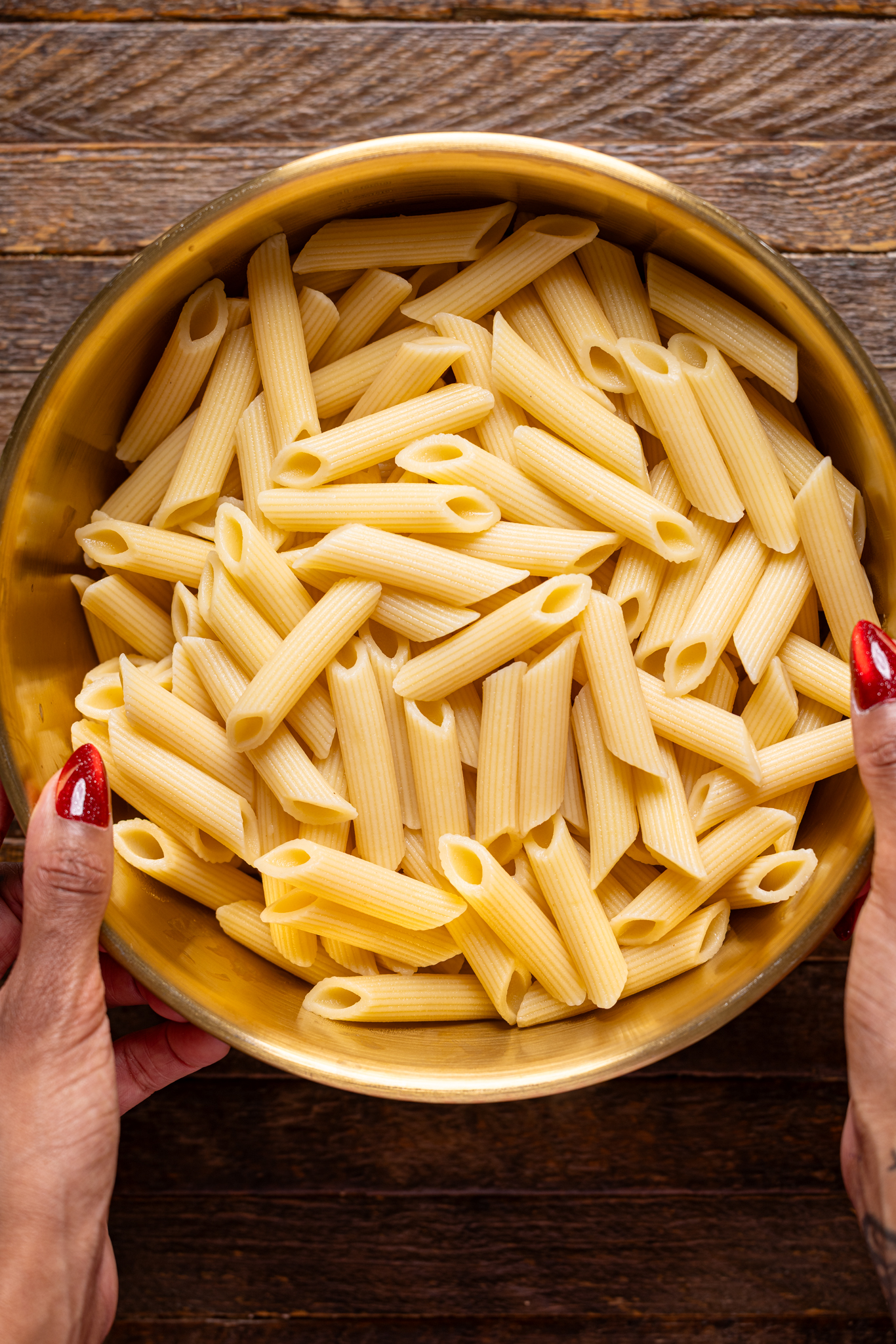 An image of cooked pasta in a gold bowl being held with hands.