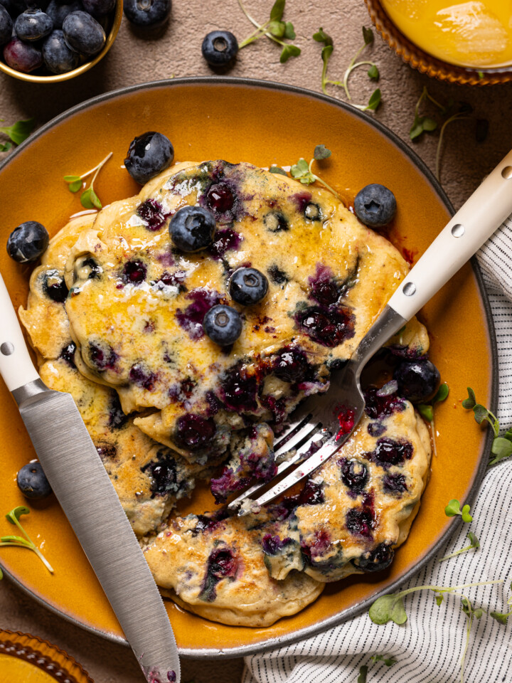 Up close shot of blueberries pancakes on a plate with knife and fork.