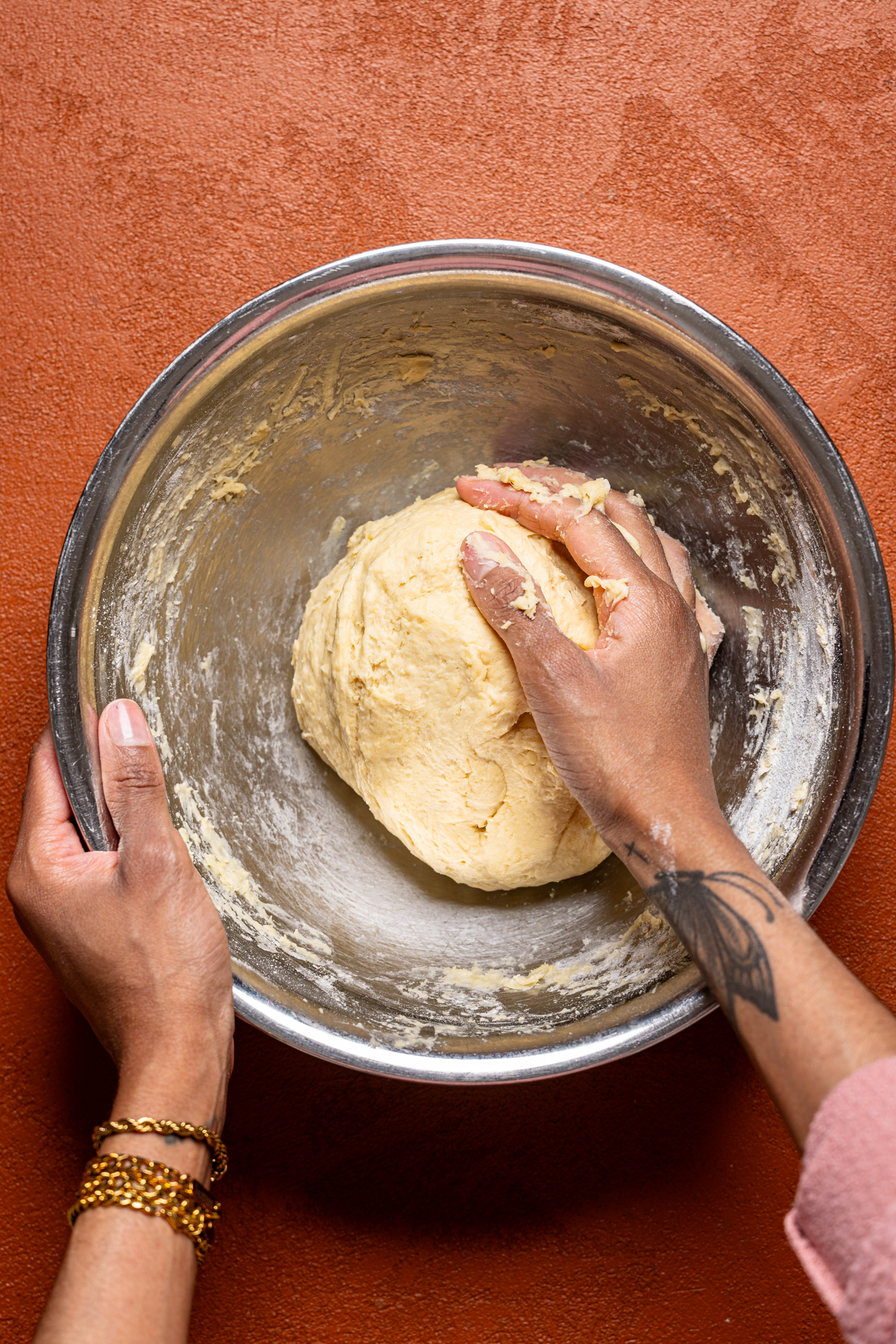 Dough in a silver bowl being kneaded by hands. 