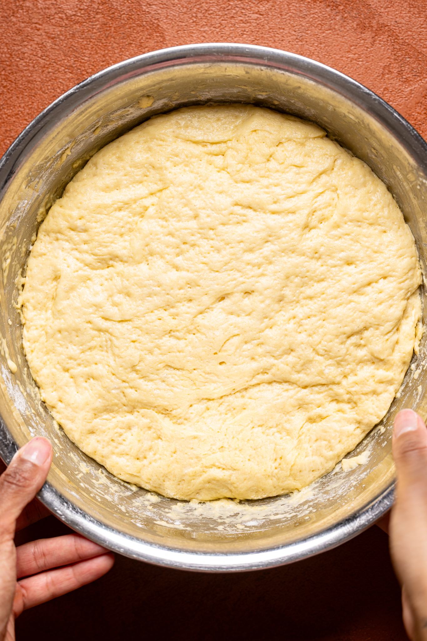 Risen dough in a silver bowl being held by female hands.