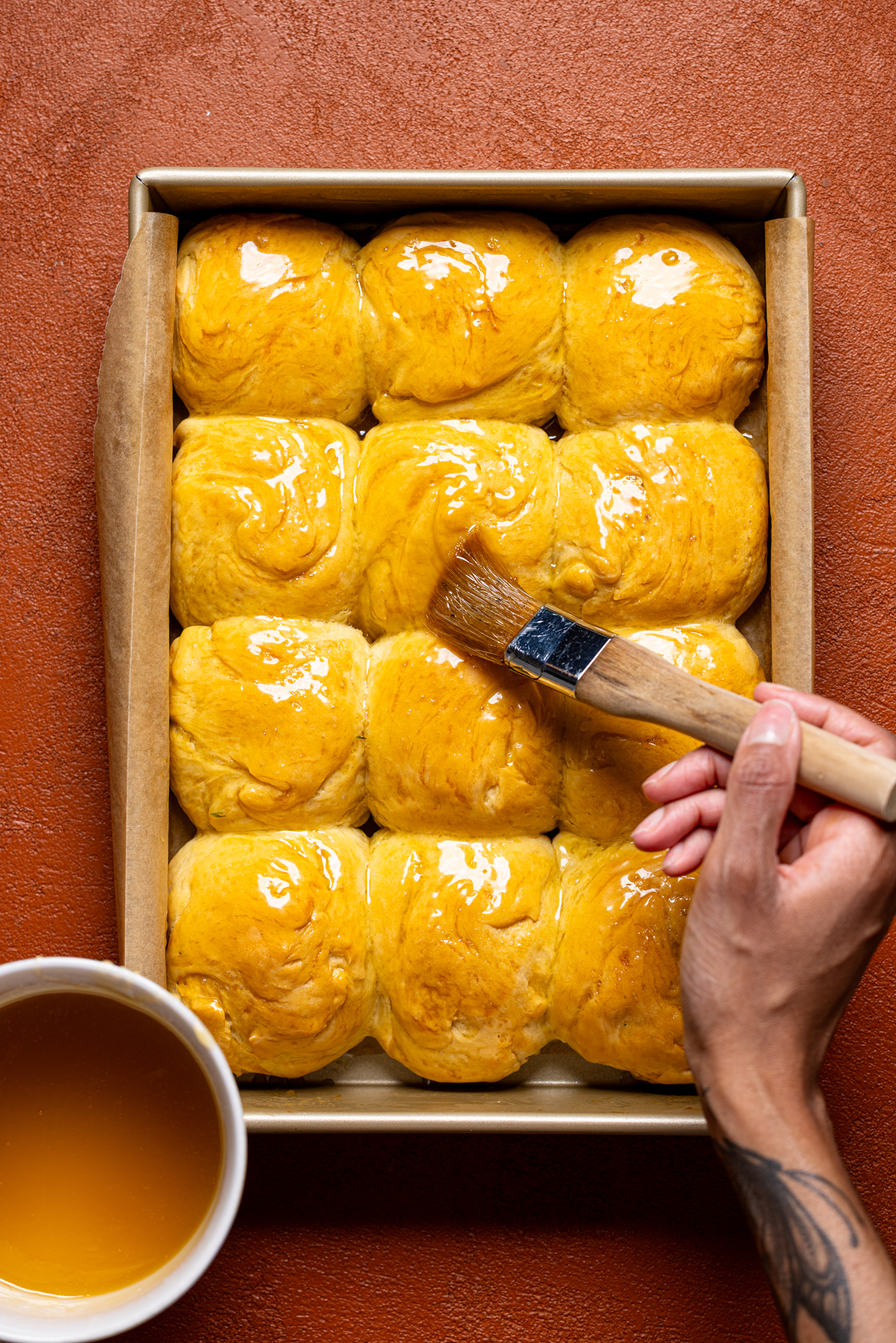 Dinner rolls being brushed with honey-butter mixture.