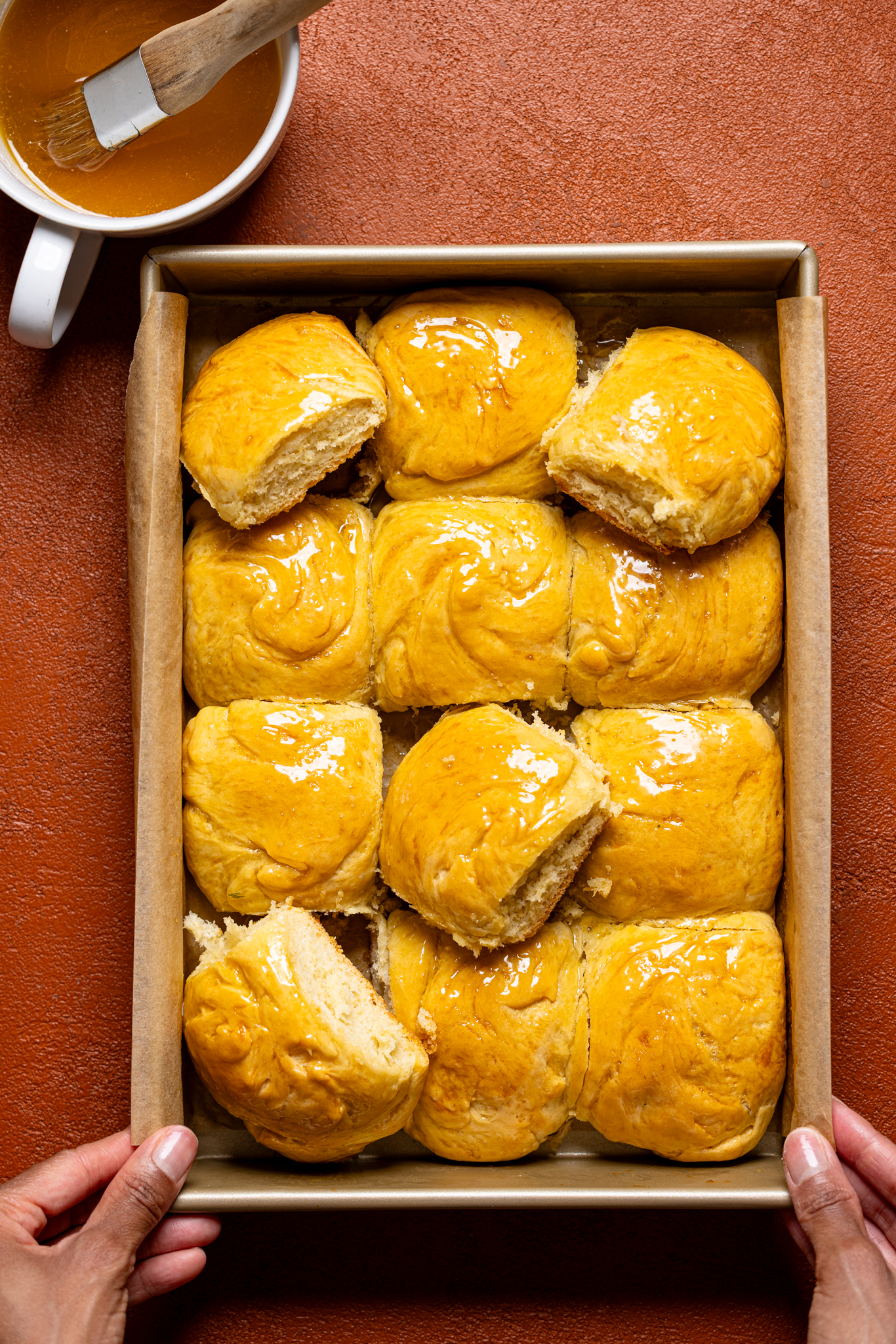 Dinner rolls being held by hand in a baking dish on a burnt orange table.