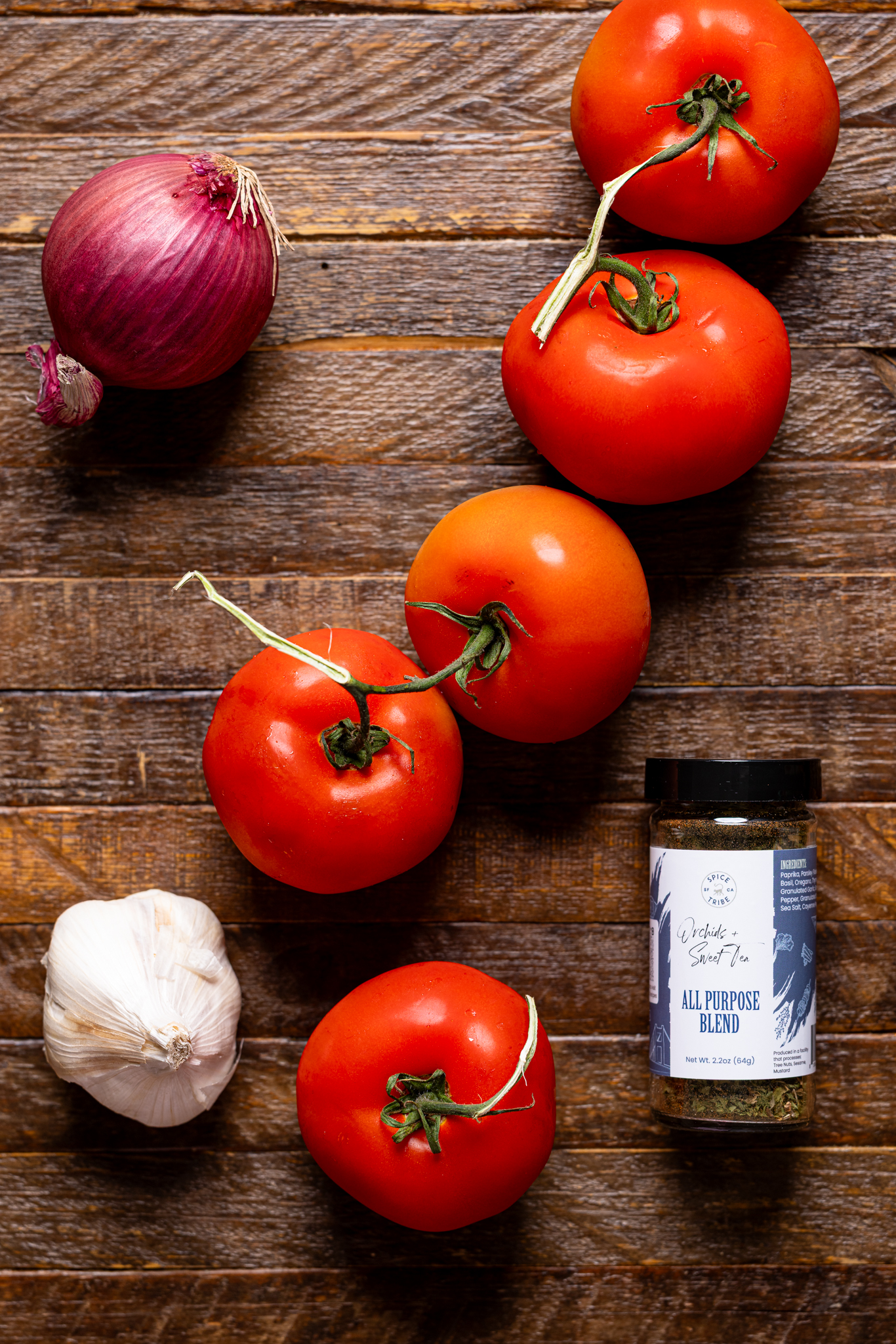 Image of tomatoes, garlic, onion, and seasoning on a brown wood table.